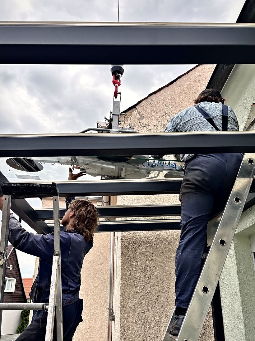 Zwei Monteure setzen eine Glasscheibe in eine Überdachung ein